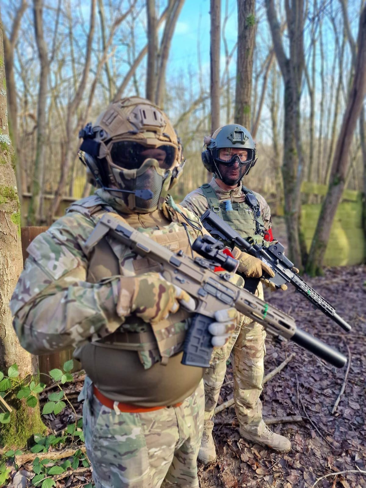 Two players in camouflage and eye protection waiting at the treeline before a game