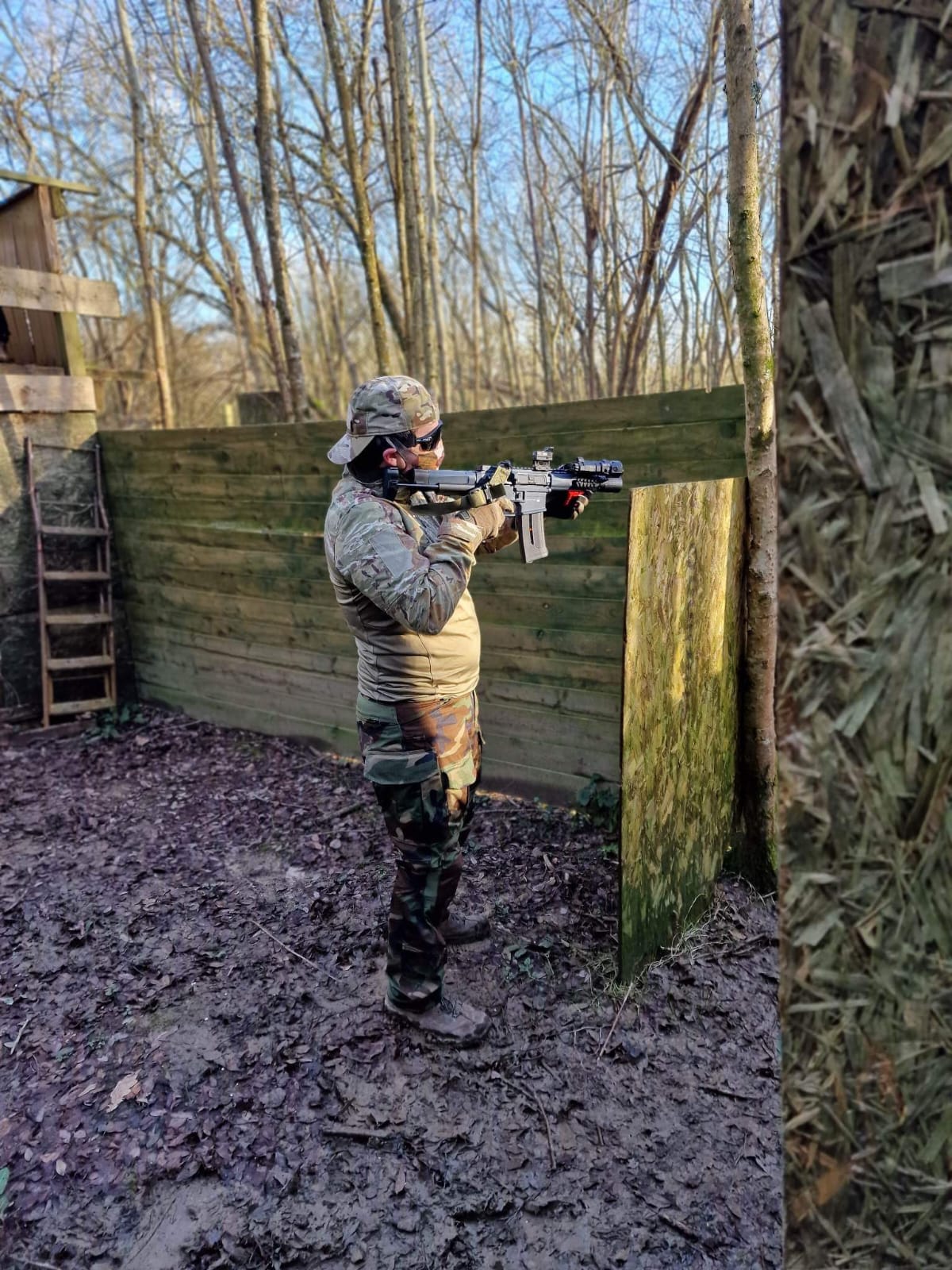 A player taking aim from behind a wooden barricade in the woodland